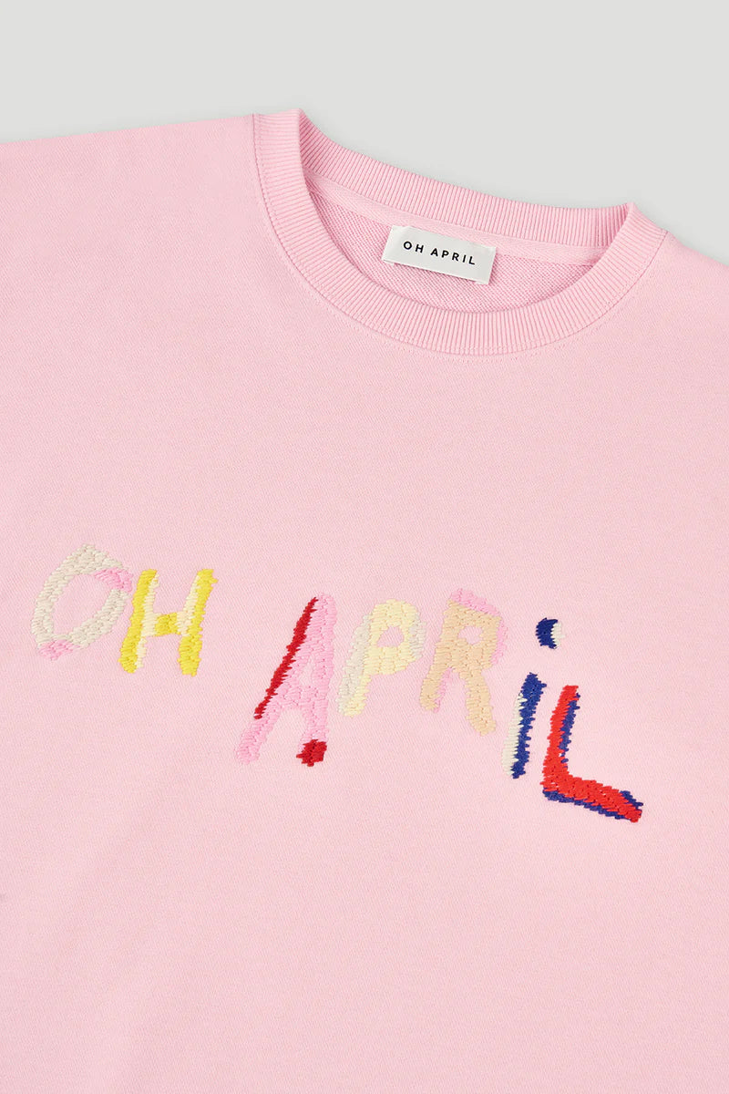 Pink sweater with colorful text 'OH APRIL' on a light gray background