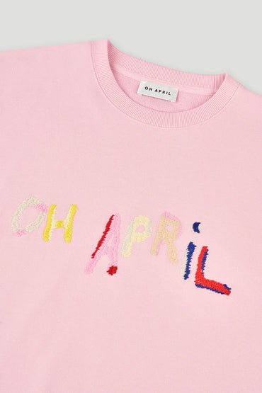 Pink sweater with colorful text 'OH APRIL' on a light gray background
