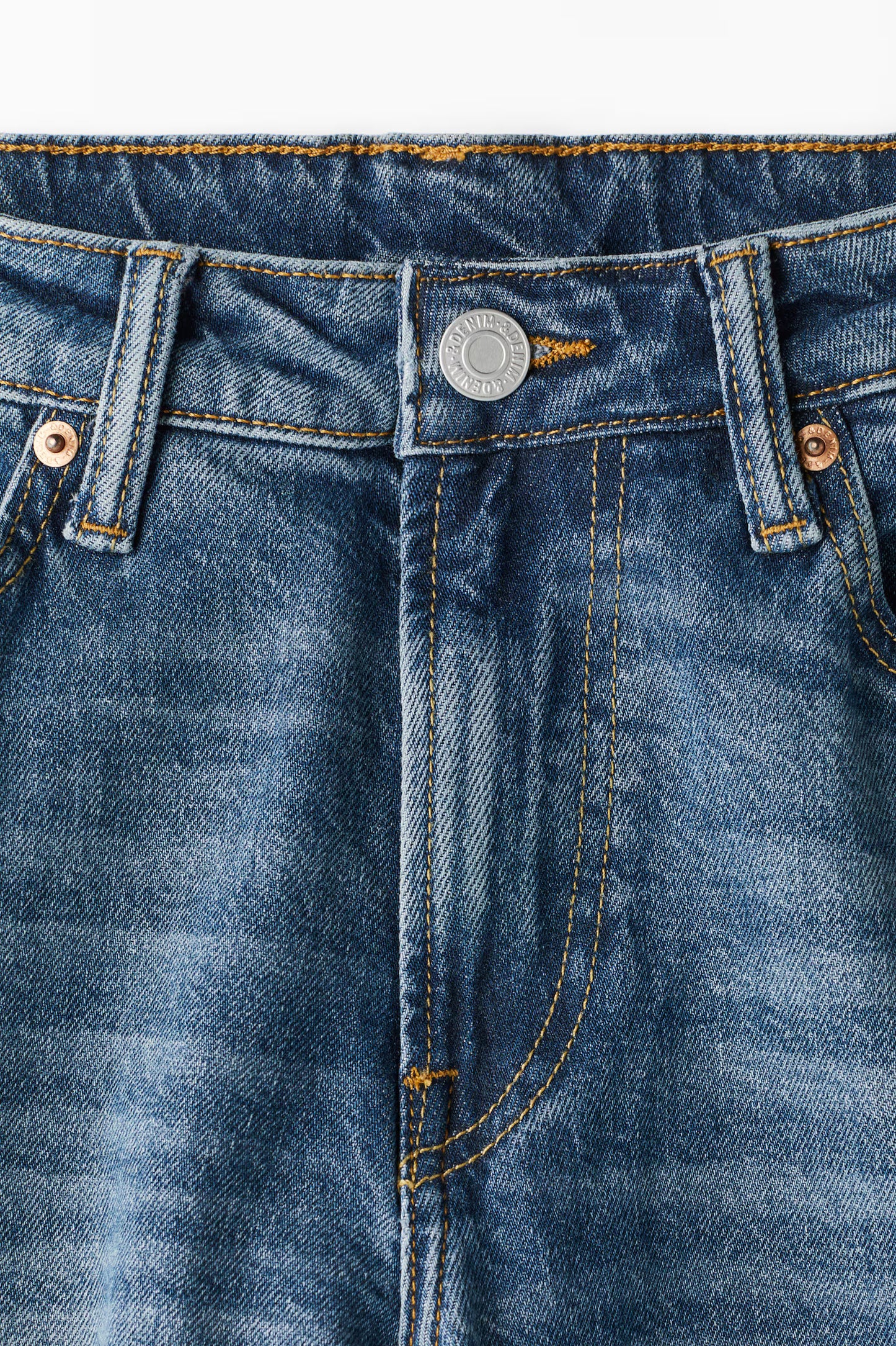 Close-up of blue denim jeans with button and stitching details on a white background