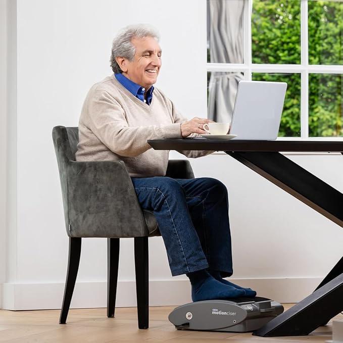 Man sitting at a table with a laptop, using a foot pedal device.