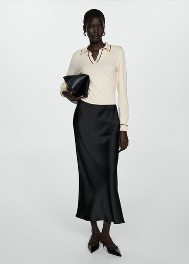 Woman wearing a cream blouse and black skirt holding a black clutch against a white background
