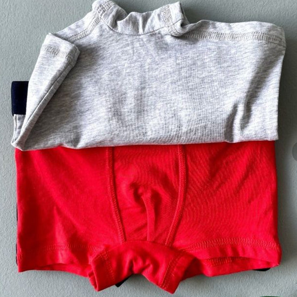 Gray top and red shorts on a gray surface with a Torob.com website open in the background.