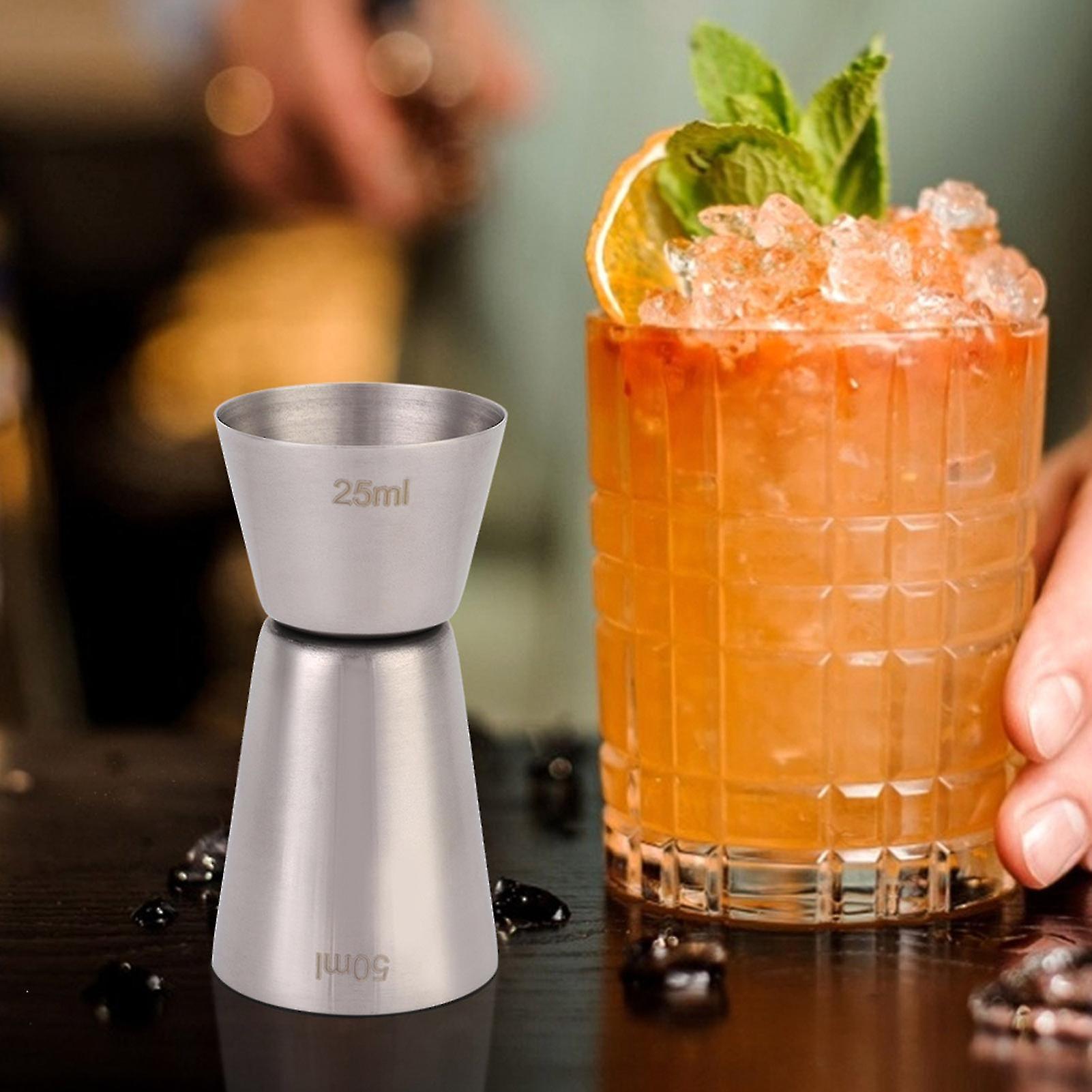 Cocktail with ice and garnish next to a metal measuring cup on a bar counter.