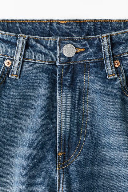 Close-up of blue denim jeans with button and stitching details on a white background