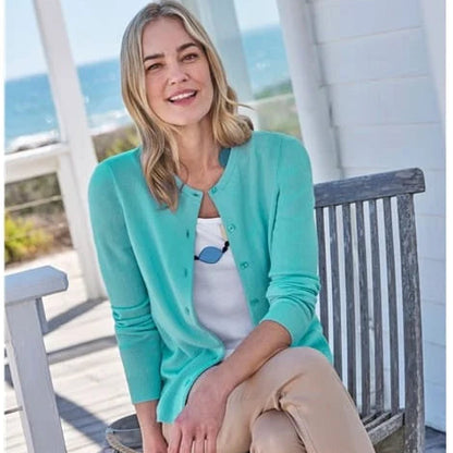 Woman sitting on a wooden bench by the sea wearing a turquoise cardigan.