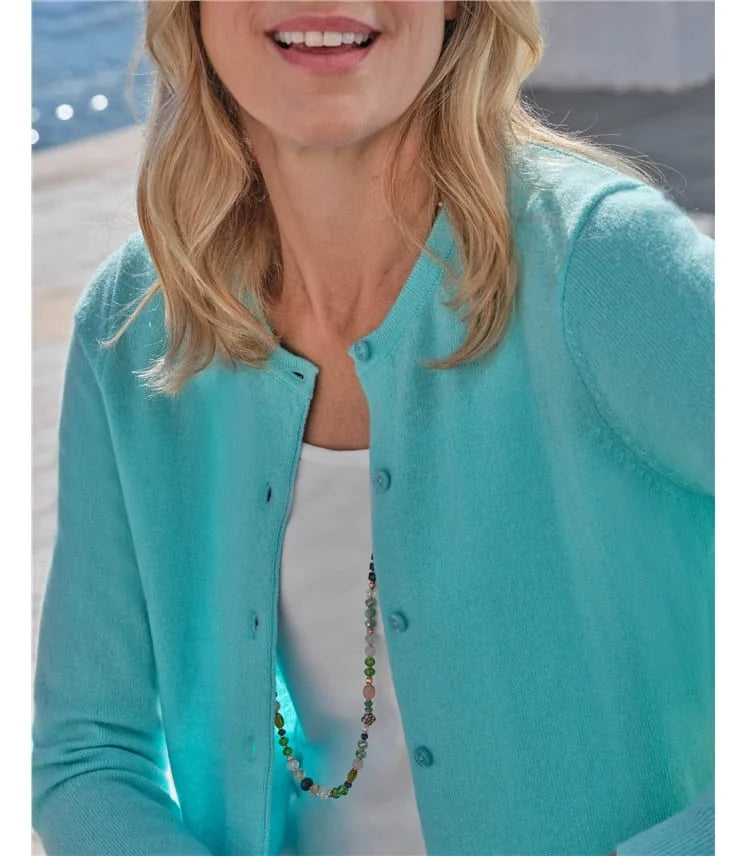 Woman wearing a turquoise cardigan over a white top with a necklace, blurred background