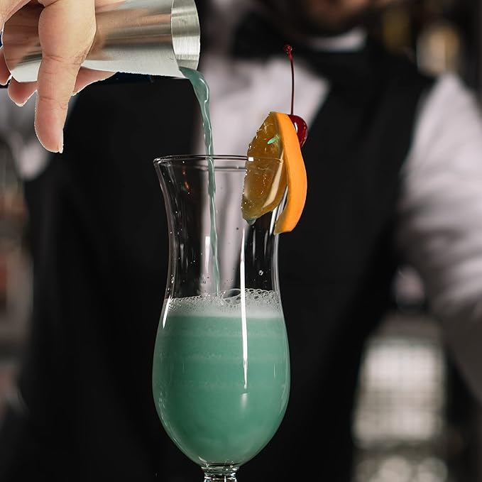 Bartender pouring a blue cocktail into a glass with a cherry and orange slice garnish.