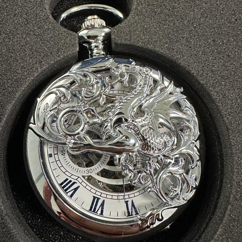 Silver pocket watch with intricate design on a black surface