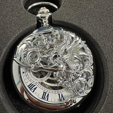 Silver pocket watch with intricate design on a black surface